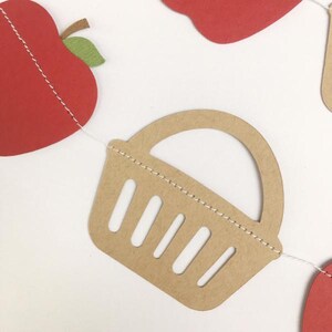 Peut inclure: Une guirlande en papier avec un panier en papier brun avec une bordure blanche cousue et une pomme rouge avec une feuille verte.