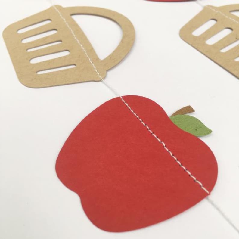 Peut inclure: Une guirlande en papier compos&eacute;e d'une pomme rouge en papier avec une feuille verte et d'un panier en papier brun avec une ficelle blanche.