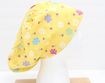 May include: Yellow surgical scrub cap with a pattern of colorful paw prints, white daisies, and pink tulips. The cap is made of a soft fabric and is designed to cover the hair during medical procedures.