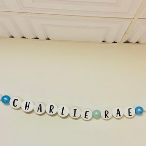 May include: A white banner with the name "CHARLIE RAE" spelled out in black letters on white circles. The banner is strung with blue and white beads and stars.
