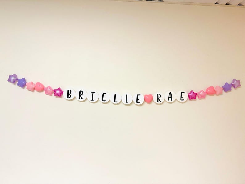 May include: A white banner with the name "Brielle Rae" spelled out in black letters. The banner is decorated with pink and purple stars and hearts.