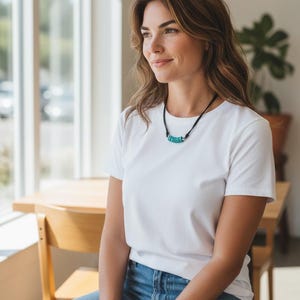 May include: A necklace featuring a black cord and a series of small, circular, turquoise-colored beads arranged horizontally at the center, accented by two small silver-toned metal spacers on either side of the bead cluster.