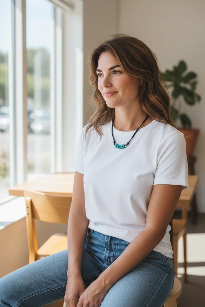 May include: A necklace featuring a black cord and a series of small, circular, turquoise-colored beads arranged horizontally at the center, accented by two small silver-toned metal spacers on either side of the bead cluster.