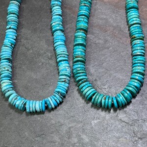May include: Two strands of turquoise beads, each with a different length, are displayed on a grey background. The beads are a light blue colour and are round and flat.