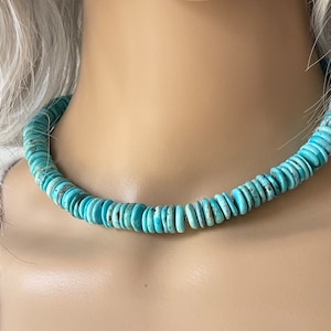 May include: A turquoise blue necklace made of round, flat beads. The necklace is on a mannequin's neck.