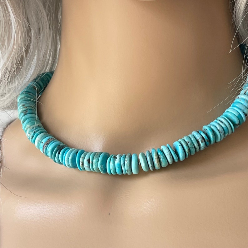 May include: A turquoise blue necklace made of round, flat beads. The necklace is on a mannequin's neck.