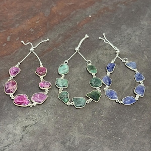 May include: Three adjustable bracelets with silver chains and gemstone beads. The bracelets feature pink, green, and blue gemstones.