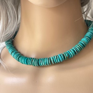 May include: A turquoise blue necklace made of round, flat beads. The necklace is on a mannequin's neck.
