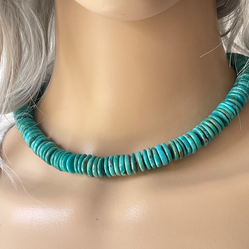 May include: A turquoise blue necklace made of round, flat beads. The necklace is on a mannequin's neck.