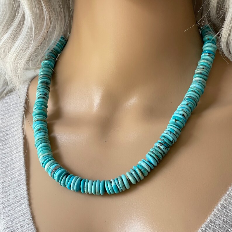 May include: A turquoise blue necklace made of round, flat beads. The necklace is on a mannequin's neck.