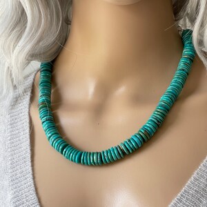 May include: A turquoise blue necklace made of round, flat beads. The necklace is on a mannequin.
