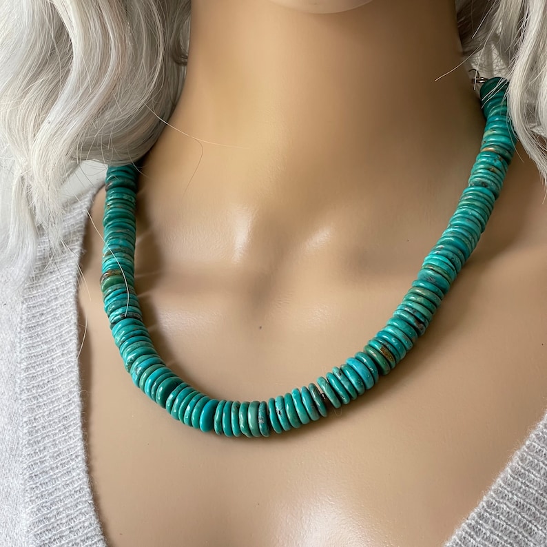 May include: A turquoise blue necklace made of round, flat beads. The necklace is on a mannequin.