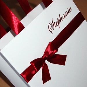 May include: White gift bag with a red satin ribbon and bow. The bag is personalized with the name "Stephanie" in cursive.