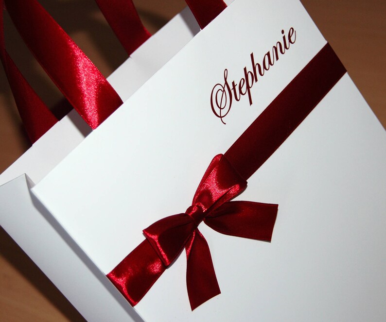 May include: White gift bag with a red satin ribbon and bow. The bag is personalized with the name "Stephanie" in cursive.