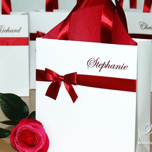 May include: White gift bags with red ribbon bows and personalized names, including "Richard", "Chris", and "Stephanie".