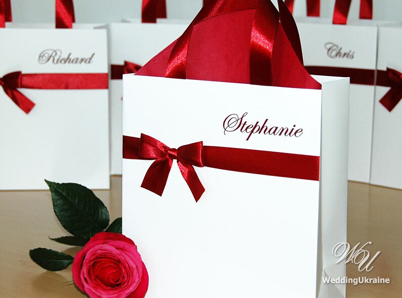 May include: White gift bags with red ribbon bows and personalized names, including "Richard", "Chris", and "Stephanie".