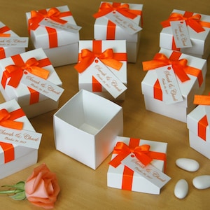 Puede incluir: Cajas de regalo blancas con cinta naranja y etiquetas que dicen "Sarah & Chuck October 20, 2017".