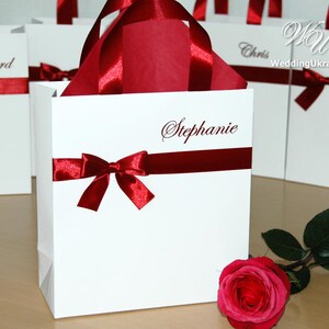 May include: White gift bags with red ribbon bows and personalized names, including "Stephanie", "Richard", and "Chris".