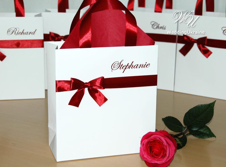 May include: White gift bags with red ribbon bows and personalized names, including "Stephanie", "Richard", and "Chris".