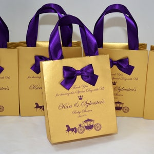 May include: Gold favor bags with purple ribbon handles and bows. The bags have a royal carriage design and the text "Thank You for sharing this Special Day with Us Kari & Sylvester's Baby Shower July 2020".