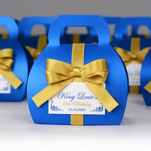 Pode incluir: Caixas de presente azuis e douradas com um laço e uma etiqueta personalizada que diz "King Louie's 18th Birthday 11.13.2021".