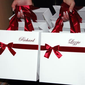 May include: Two white gift bags with red ribbon bows and personalized names, "Richard" and "Lizzie", printed in cursive.