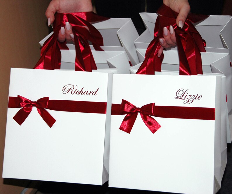 May include: Two white gift bags with red ribbon bows and personalized names, "Richard" and "Lizzie", printed in cursive.