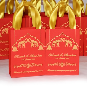 Op de afbeelding: Rode en gouden cadeauzakjes met een ontwerp van twee olifanten die elkaar aankijken. De zakjes hebben gouden handvatten en de tekst "Kamesh & Shambavi 31st January 2021" erop gedrukt.