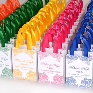Könnte beinhalten: Eine Sammlung kleiner weißer Geschenktüten mit bunten Satinbandgriffen. Die Taschen sind mit einem Paisley-Muster und dem Text "Mehendi Night" mit dem Datum "03.19.2020" verziert.