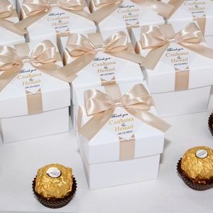Könnte beinhalten: Weiße Geschenkboxen mit einem beigefarbenen Band und Schleife. Jede Box hat ein personalisiertes Etikett mit dem Text "Danke Slađana & Nenad 05.15.2021".