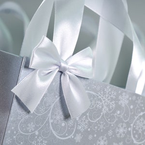 May include: A silver gift bag with a white satin bow and snowflake pattern.