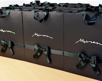 May include: A row of black gift bags with black ribbon bows and the word "Murren" written in white on the front of each bag.