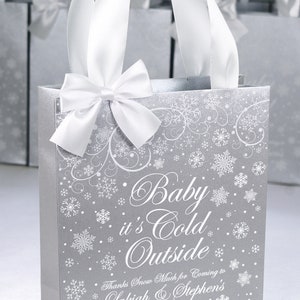 May include: Silver gift bag with white snowflake pattern and white satin ribbon bow. The bag has the text "Baby it's Cold Outside" and "Thanks Snow Much for Coming to Lakiah & Stephen's Baby Shower".