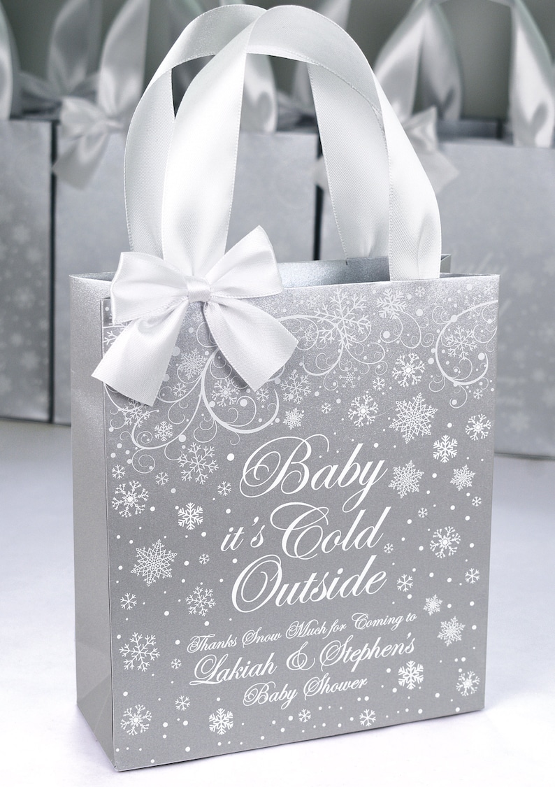 May include: Silver gift bag with white snowflake pattern and white satin ribbon bow. The bag has the text "Baby it's Cold Outside" and "Thanks Snow Much for Coming to Lakiah & Stephen's Baby Shower".