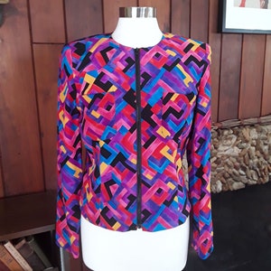 May include: A black, purple, red, blue, and yellow geometric patterned jacket with a black zipper.
