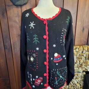 May include: Black knitted cardigan with a red trim and various winter-themed embroidered details, including snowflakes, trees, a snowman, a hat, and skis.