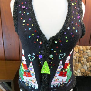 May include: Black Christmas sweater vest with a zipper closure and a festive design featuring two Christmas trees, candy canes, and Santa Claus figures. The vest is decorated with sequins and colorful beads.