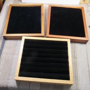 May include: Three wooden ring boxes with black velvet interiors. The boxes are different sizes and have a natural wood finish.