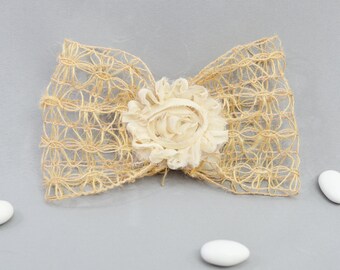 May include: A beige burlap bow with a white fabric flower in the center. The bow is tied with a knot and the flower is made of several layers of fabric.