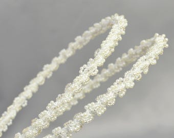 May include: Two white beaded headbands with a delicate floral design. The headbands are made of small white beads that are strung together to create a delicate and intricate pattern.