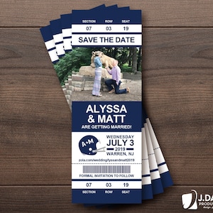May include: A blue and white save the date card designed to look like a ticket. The card features a photo of a couple in front of a statue of a lion. The text on the card reads "Save the Date", "Alyssa & Matt", "Are Getting Married!" and "Wednesday July 3, 2019 Warren, NJ".