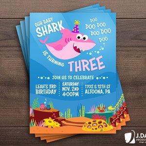 May include: A blue and orange birthday invitation with a pink cartoon shark wearing a party hat. The text reads "Our Baby Shark is Turning Three" and includes details for the party, including the date, time, and location.