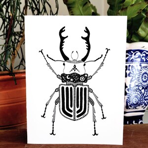May include: Black and white line art illustration of a stag beetle with intricate details. The beetle has a large, ornate head with long, curved mandibles and a segmented body with a pattern of stripes and dots.
