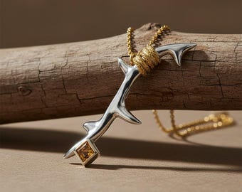 May include: A silver pendant shaped like a thorny branch with a textured gold-toned coil at the top and a square-cut amber-colored gemstone at the base. The pendant hangs from a delicate gold-toned chain, featuring a polished metallic finish.