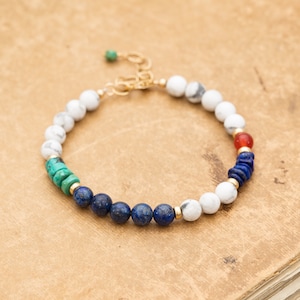 May include: A gold bracelet with white, blue, green, and red gemstone beads. The bracelet has a gold clasp.