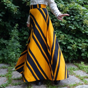Può includere: Lunga gonna fluida con un audace motivo a righe diagonali gialle e blu navy. La gonna è abbinata a una camicetta bianca. Il design della gonna crea un effetto visivo sorprendente, adatto a varie occasioni.
