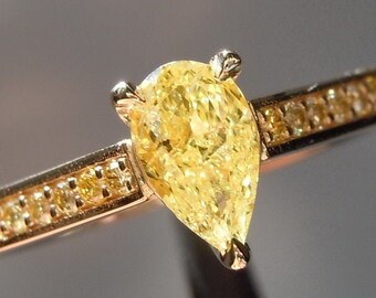 May include: A gold ring with a pear-shaped yellow diamond set in the center. The band is adorned with smaller yellow diamonds.