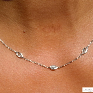 Puede incluir: Un delicado collar de plata con múltiples diamantes en forma de marquesa. Los diamantes están espaciados uniformemente a lo largo de una fina cadena, creando un diseño minimalista y elegante. El collar se muestra sobre un fondo de tono de piel.