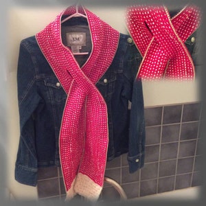 May include: A pink and white knitted scarf with a white border. The scarf is folded and draped over a denim jacket.
