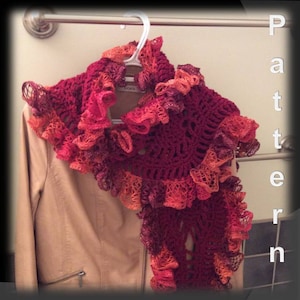 May include: A crocheted shawl with a ruffled edge in shades of red, orange, and brown. The shawl is draped over a tan jacket.